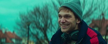 Movie still from “A Night at the Kindergarten” (2022), directed by Rafal Skalski – A person wearing headphones and a beanie; Close Up shot, Low angle