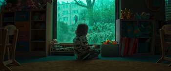 Movie still from “A Night at the Kindergarten” (2022), directed by Rafal Skalski – A little boy sitting on the floor looking out of a window; Wide shot, Over the shoulder angle