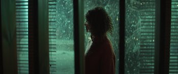 Movie still from “A Night at the Kindergarten” (2022), directed by Rafal Skalski – A woman standing in front of a window looking outside; Medium shot, Low angle