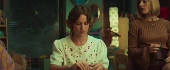 Movie still from “A Night at the Kindergarten” (2022), directed by Rafal Skalski – A woman in a white sweater looking down at her cell phone; Medium shot, Low angle