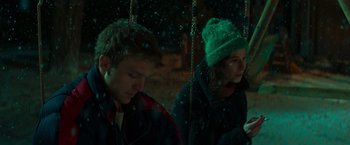 Movie still from “A Night at the Kindergarten” (2022), directed by Rafal Skalski – A man and a woman sitting on a swing in the snow; Medium shot, Low angle