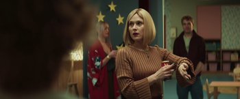 Movie still from “A Night at the Kindergarten” (2022), directed by Rafal Skalski – A woman in a brown sweater is holding a cup; Medium shot, Over the shoulder angle