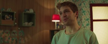 Movie still from “A Night at the Kindergarten” (2022), directed by Rafal Skalski – A young man is standing in front of a lamp in a living room; Close Up shot, Over the shoulder angle