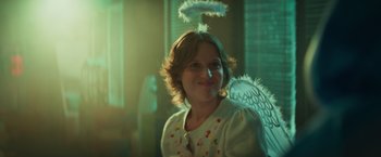 Movie still from “A Night at the Kindergarten” (2022), directed by Rafal Skalski – A woman wearing a white angel costume with a white feather halo on her head; Close Up shot, Over the shoulder angle