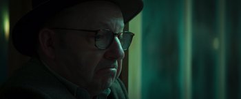 Movie still from “A Night at the Kindergarten” (2022), directed by Rafal Skalski – An older man wearing glasses and a hat looking out of a window; Close Up shot, Over the shoulder angle