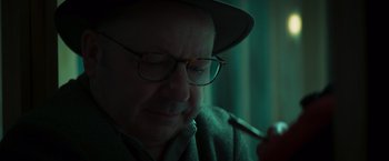 Movie still from “A Night at the Kindergarten” (2022), directed by Rafal Skalski – An older man wearing glasses and a hat is smoking a pipe; Close Up shot, Low angle