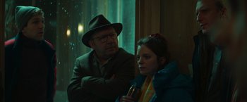 Movie still from “A Night at the Kindergarten” (2022), directed by Rafal Skalski – An older man and a young woman sitting next to each other in front of a window; Close Up shot, Over the shoulder angle
