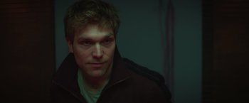 Movie still from “A Night at the Kindergarten” (2022), directed by Rafal Skalski – A person wearing a black jacket; Close Up shot, High angle