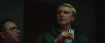 Movie still from “A Night at the Kindergarten” (2022), directed by Rafal Skalski – A man holding a paper cup in his hand; Close Up shot, Low angle