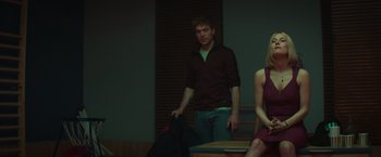 Movie still from “A Night at the Kindergarten” (2022), directed by Rafal Skalski – A man and a woman standing in front of a wooden table; Medium shot, Low angle