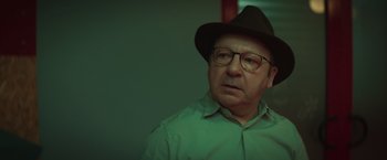 Movie still from “A Night at the Kindergarten” (2022), directed by Rafal Skalski – An older man wearing glasses and a hat; Close Up shot, Over the shoulder angle