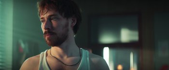 Movie still from “A Night at the Kindergarten” (2022), directed by Rafal Skalski – A person with a beard wearing a necklace; Close Up shot, Low angle