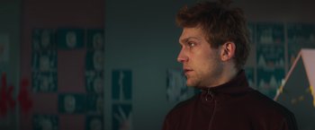 Movie still from “A Night at the Kindergarten” (2022), directed by Rafal Skalski – A young man looking to his left while wearing a jacket; Close Up shot, Low angle
