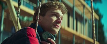 Movie still from “A Night at the Kindergarten” (2022), directed by Rafal Skalski – A young man wearing a red jacket is holding his headphones; Close Up shot, Low angle