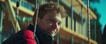 Movie still from “A Night at the Kindergarten” (2022), directed by Rafal Skalski – A young man with headphones hanging from a rope; Close Up shot, Low angle
