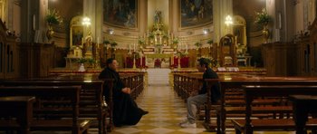 Two men sitting in a church with a large altar in the background