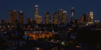 Movie still from “A Perfect Pairing” (2022), directed by Stuart McDonald – A view of a city skyline at night with buildings lit up; Extreme Wide shot, High angle