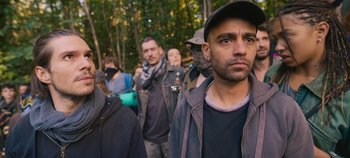 Movie still from “A Place to Fight For” (2023), directed by Romain Cogitore – A group of people standing in a forest; Close Up shot, Over the shoulder angle