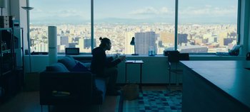 Movie still from “A Place to Fight For” (2023), directed by Romain Cogitore – A man sitting in front of a large window looking out at a city; Wide shot, High angle