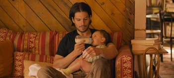 Movie still from “A Place to Fight For” (2023), directed by Romain Cogitore – A man holding a baby while holding a bottle of milk; Medium shot, High angle