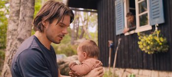 Movie still from “A Place to Fight For” (2023), directed by Romain Cogitore – A man holding a baby in his arms outside; Close Up shot, Over the shoulder angle