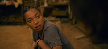 Movie still from “A Place to Fight For” (2023), directed by Romain Cogitore – A young woman sitting on the ground looking at the camera; Close Up shot, Over the shoulder angle