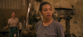 Movie still from “A Place to Fight For” (2023), directed by Romain Cogitore – A young woman with tattoos is standing in front of a stone wall; Close Up shot, Over the shoulder angle