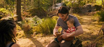 Movie still from “A Place to Fight For” (2023), directed by Romain Cogitore – A man and a baby are sitting in the grass; Medium shot, High angle