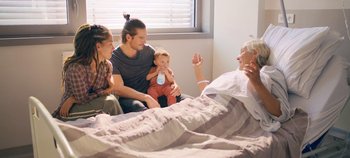 Movie still from “A Place to Fight For” (2023), directed by Romain Cogitore – A group of people sitting on top of a bed next to each other; Wide shot, Over the shoulder angle