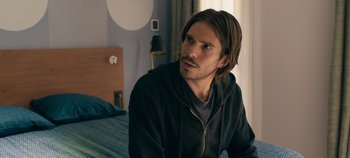 Movie still from “A Place to Fight For” (2023), directed by Romain Cogitore – A man sitting on top of a bed in front of a window; Close Up shot, Over the shoulder angle