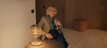 Movie still from “A Place to Fight For” (2023), directed by Romain Cogitore – A woman sitting on a chair holding a glass of wine; Medium shot, Over the shoulder angle