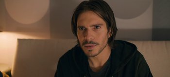 Movie still from “A Place to Fight For” (2023), directed by Romain Cogitore – A person with long hair and a beard; Close Up shot, Over the shoulder angle