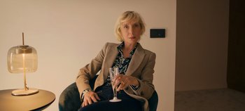 Movie still from “A Place to Fight For” (2023), directed by Romain Cogitore – A woman sitting in a chair holding a glass of wine; Close Up shot, Over the shoulder angle