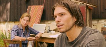 Movie still from “A Place to Fight For” (2023), directed by Romain Cogitore – A man with long brown hair sitting in front of a laptop; Close Up shot, Over the shoulder angle