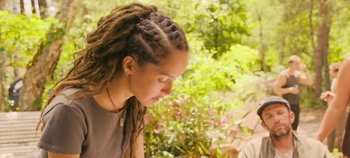 Movie still from “A Place to Fight For” (2023), directed by Romain Cogitore – A woman with dreads is looking down at a tree; Close Up shot, Over the shoulder angle