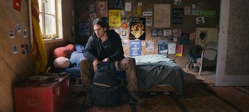 Movie still from “A Place to Fight For” (2023), directed by Romain Cogitore – A man sitting on a bed with a backpack; Medium shot, Over the shoulder angle
