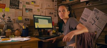 Movie still from “A Place to Fight For” (2023), directed by Romain Cogitore – A woman sitting in front of a computer on top of a desk; Medium shot, Low angle