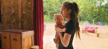 Movie still from “A Place to Fight For” (2023), directed by Romain Cogitore – A woman holding a baby in her arms outside; Medium shot, Over the shoulder angle