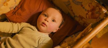 Movie still from “A Place to Fight For” (2023), directed by Romain Cogitore – A baby is laying in a bed looking at the camera; Close Up shot, Overhead angle
