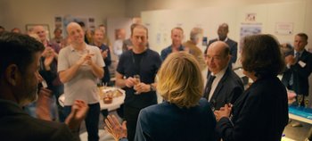 Movie still from “A Place to Fight For” (2023), directed by Romain Cogitore – A group of people standing around a room talking to each other; Medium shot, Over the shoulder angle