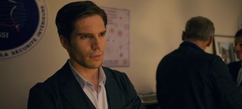 Movie still from “A Place to Fight For” (2023), directed by Romain Cogitore – A man wearing a suit and tie sitting in front of a whiteboard; Close Up shot, Over the shoulder angle