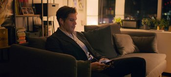 Movie still from “A Place to Fight For” (2023), directed by Romain Cogitore – A man sitting on top of a couch while holding a cell phone; Medium shot, High angle