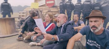 Movie still from “A Place to Fight For” (2023), directed by Romain Cogitore – A group of people sitting on the ground with papers; Medium shot, Over the shoulder angle
