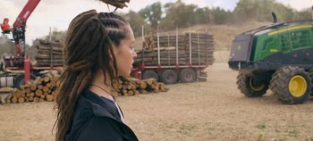 Movie still from “A Place to Fight For” (2023), directed by Romain Cogitore – A woman with dreadlocks standing in front of a truck full of logs; Close Up shot, Over the shoulder angle