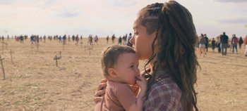 Movie still from “A Place to Fight For” (2023), directed by Romain Cogitore – A woman holding a baby in her arms in a field; Medium shot, Over the shoulder angle