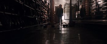 Movie still from “A Quiet Place” (2018), directed by John Krasinski – A person is walking in a room filled with stacks of books; Wide shot, Low angle