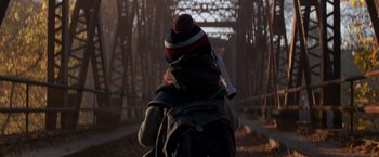 Movie still from “A Quiet Place” (2018), directed by John Krasinski – A person with a backpack walking across a bridge; Medium shot, Over the shoulder angle