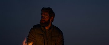 Movie still from “A Quiet Place” (2018), directed by John Krasinski – A man with a beard is sitting in the dark; Medium shot, Low angle