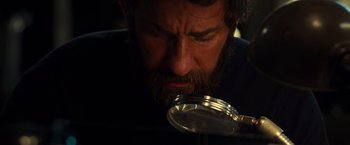 Movie still from “A Quiet Place” (2018), directed by John Krasinski – A bearded man looking at something through a magnifying glass; Close Up shot, Over the shoulder angle