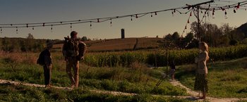Movie still from “A Quiet Place” (2018), directed by John Krasinski – A man standing on a dirt road next to a field; Wide shot, Over the shoulder angle